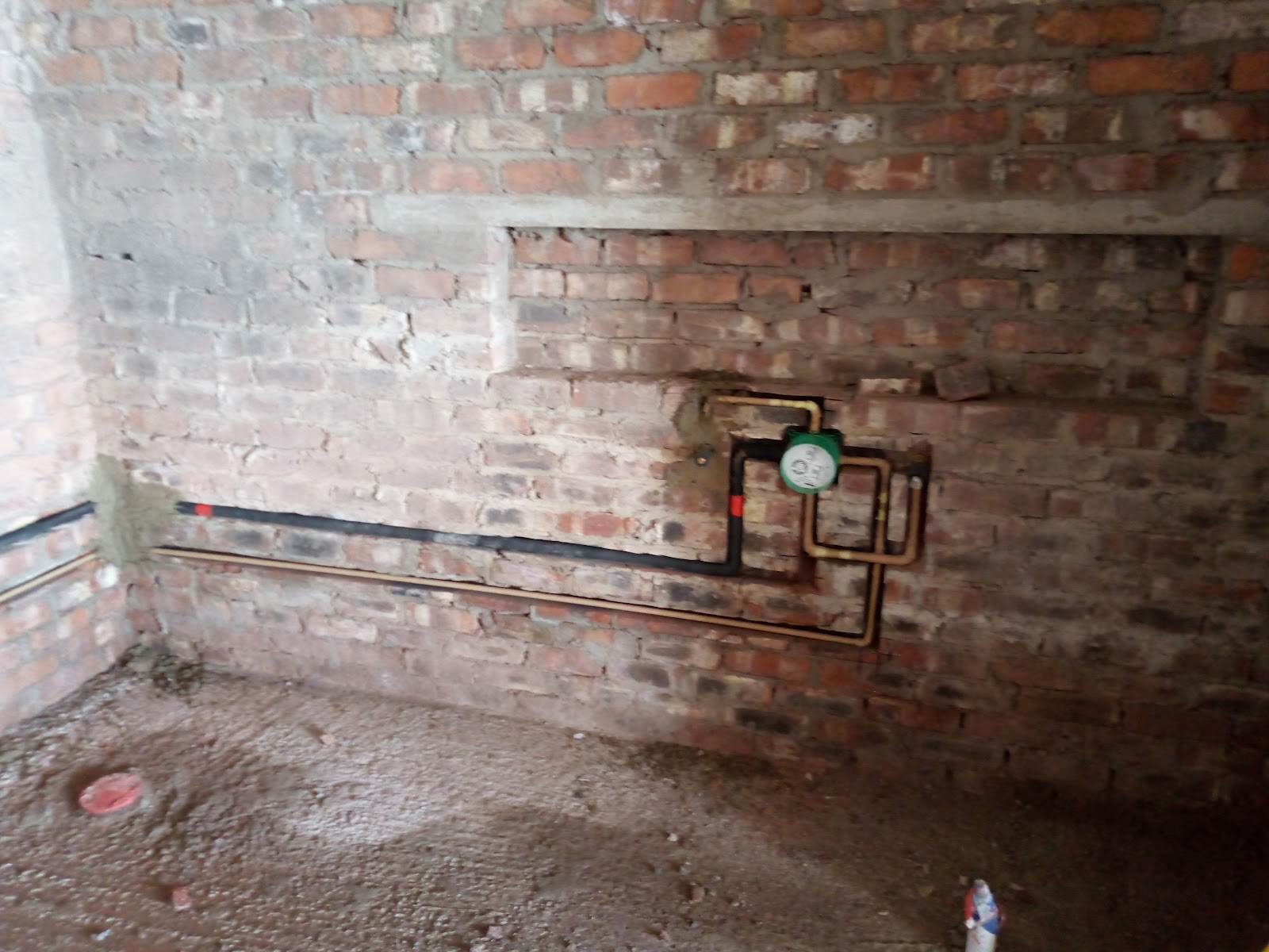 Brick basement wall with copper pipe, gauge meter, and electrical wiring installed.