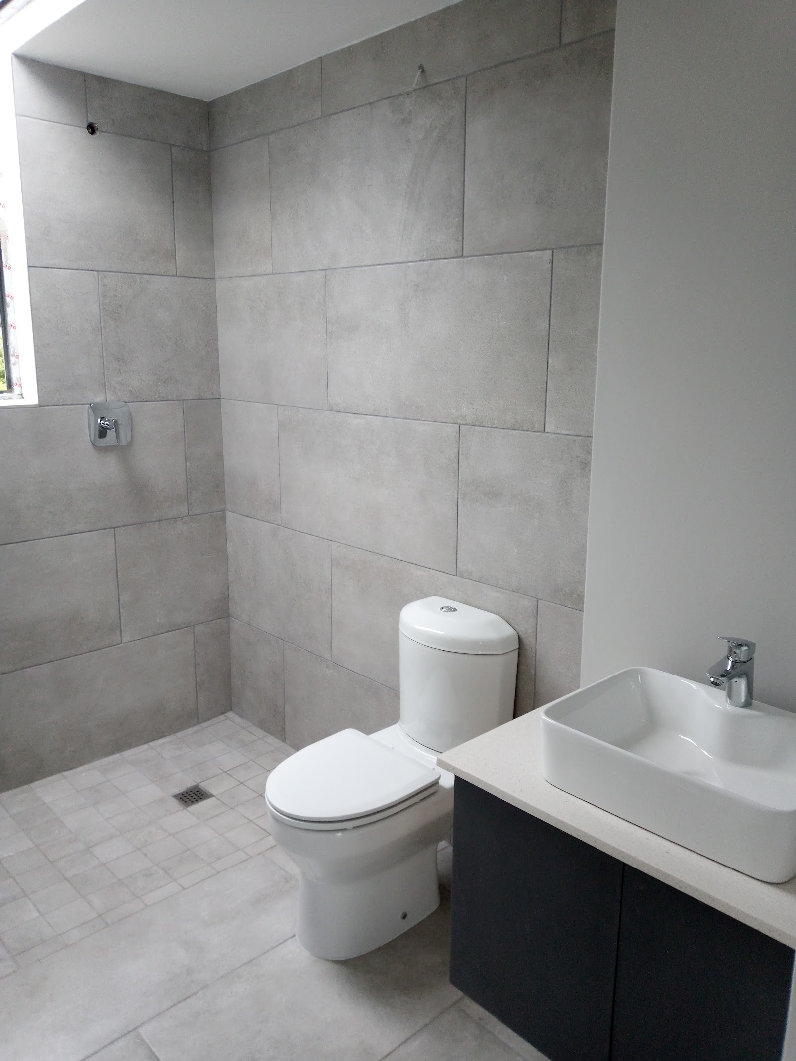 Completed bathroom with gray tile walls, white toilet, vessel sink, and skylight window.