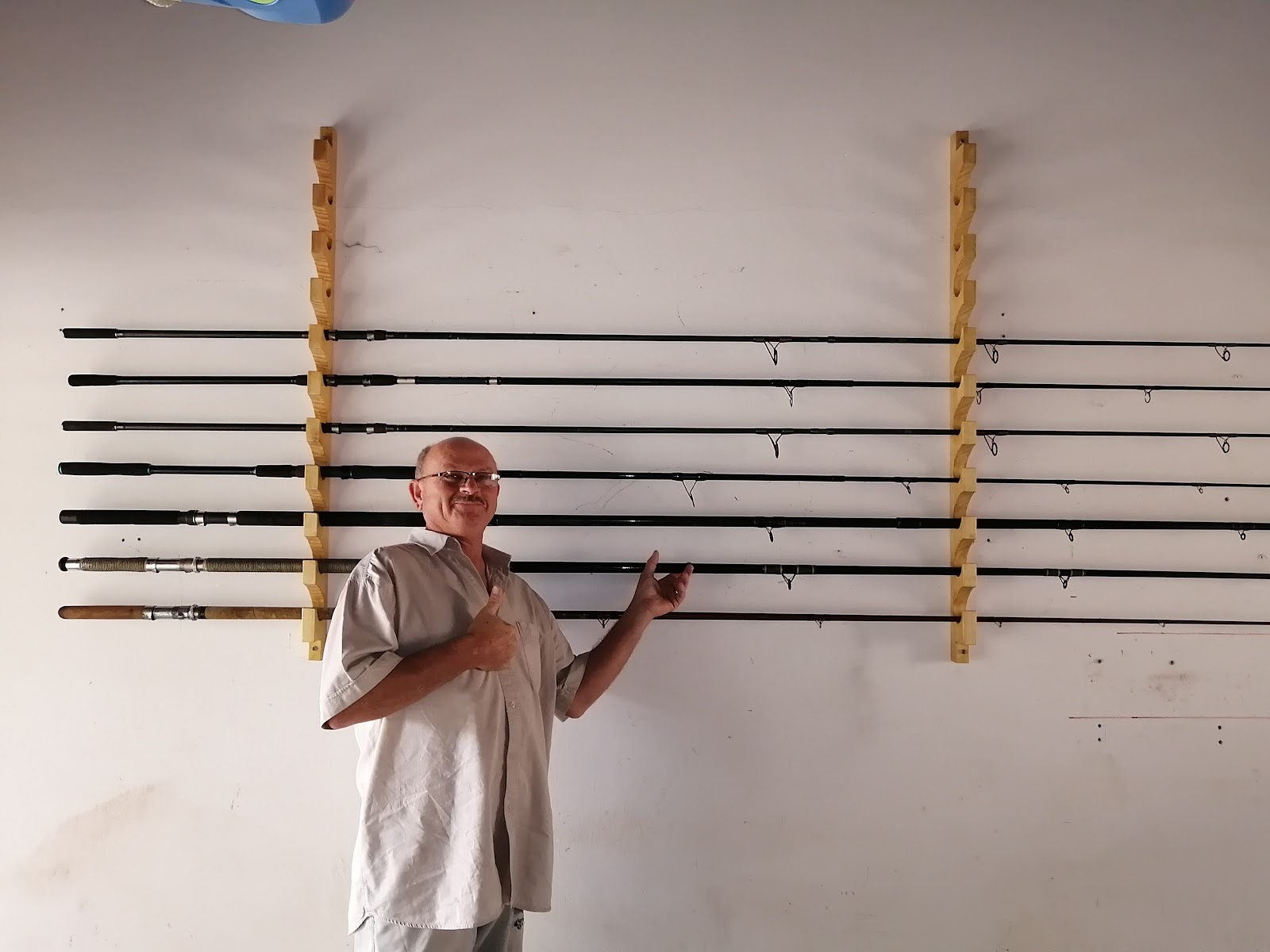 Male staff member displaying fishing rods mounted on wooden wall brackets in workshop setting.