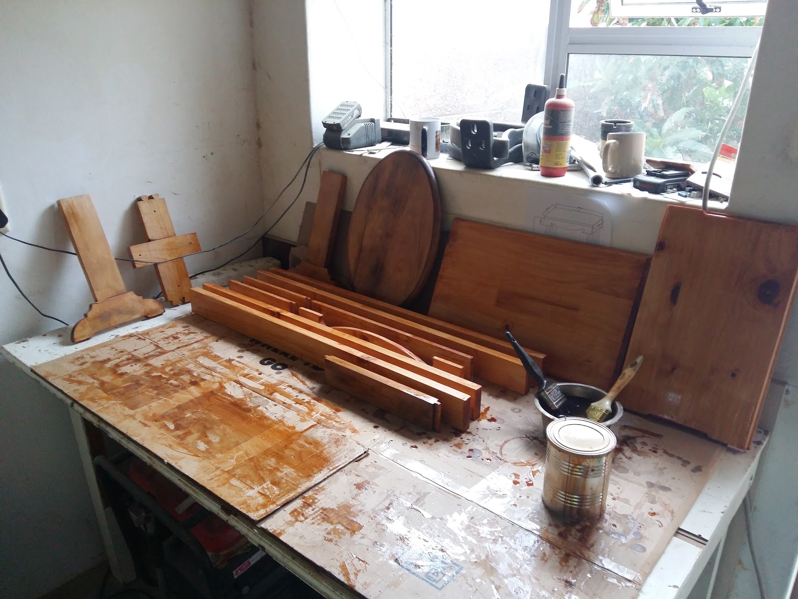 Workshop interior with wooden furniture pieces, paint supplies, and window workstation with natural light.