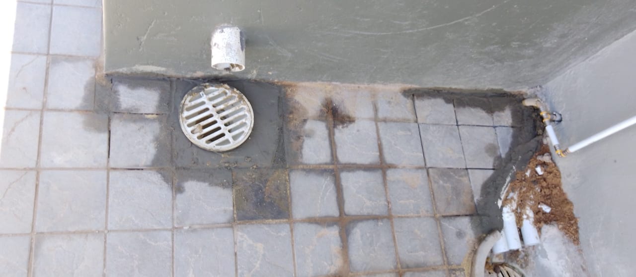 Close-up of tiled floor with drainage grate and PVC pipe installation showing construction detail work.