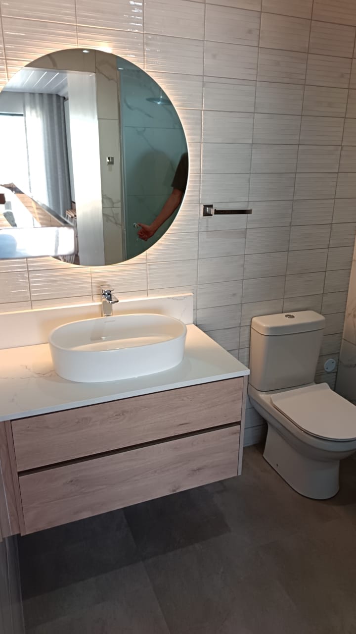 Completed bathroom with round LED mirror, white vessel sink, wooden vanity, and white toilet.
