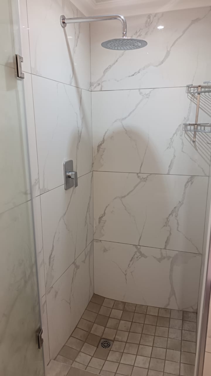 Finished shower with marble-pattern tile walls, glass enclosure, overhead rainfall showerhead, and drain.