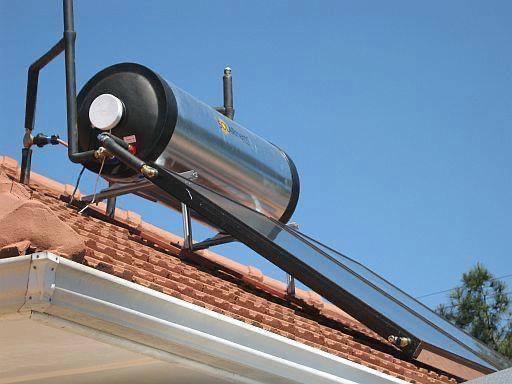Solar water heater panel mounted on corrugated metal roof with blue sky background.
