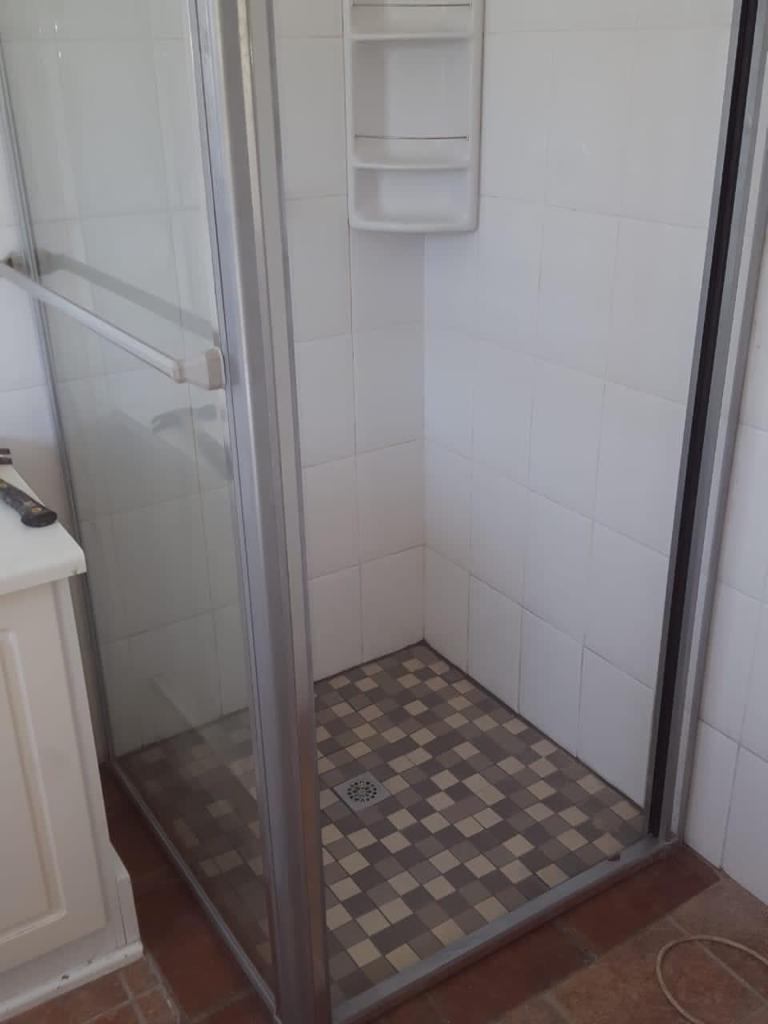 White tiled shower stall with glass enclosure and floor drain installed.