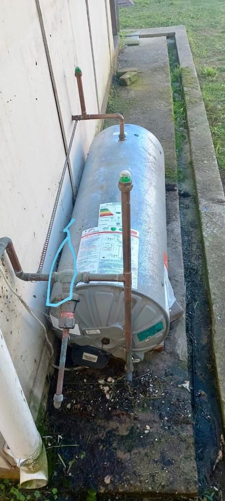 Blue water tank with regulatory label positioned against white wall in narrow space.