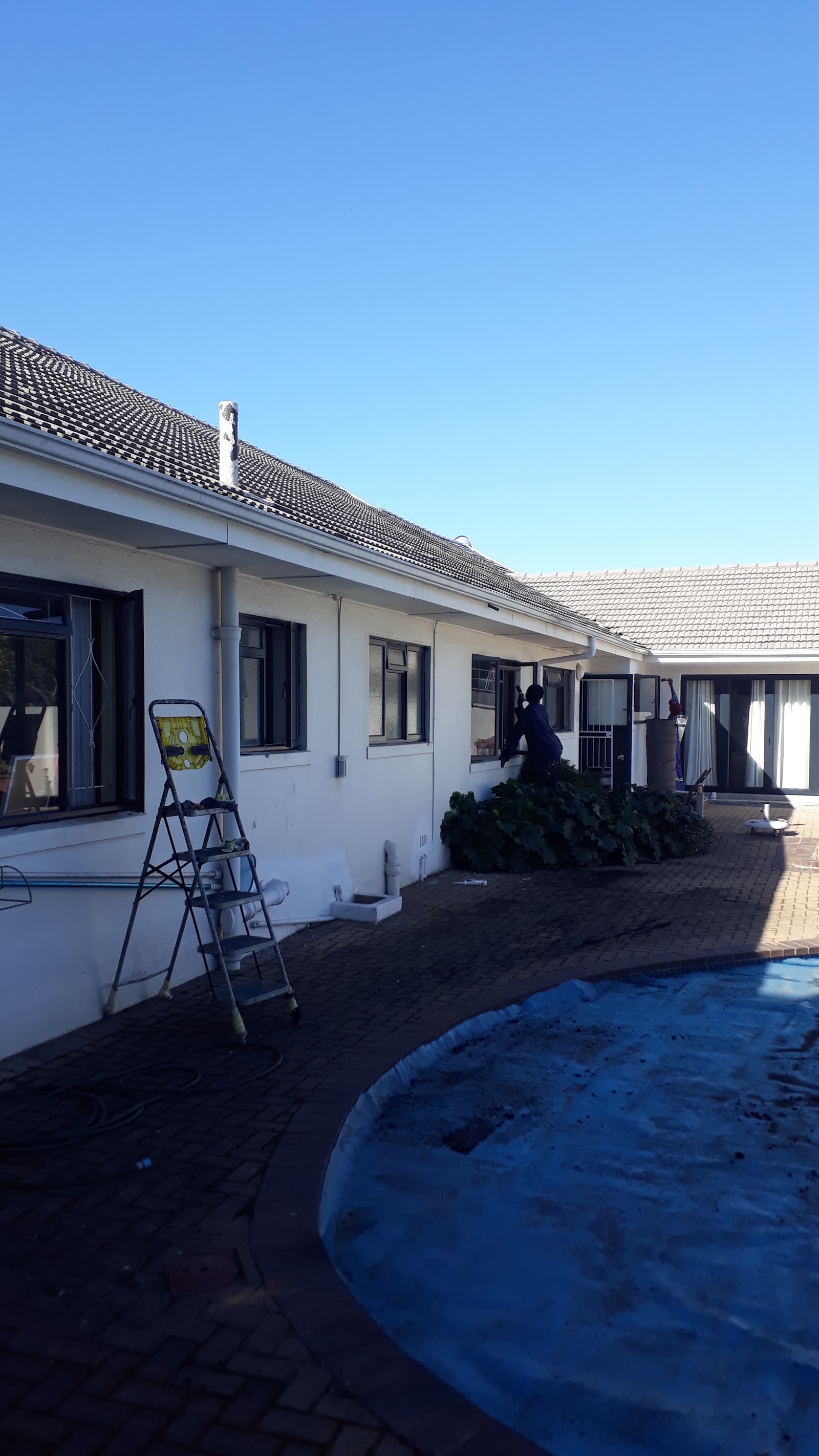 Residential property exterior showing white rendered walls, black-framed windows, pool cover, ladder during construction/renovation.