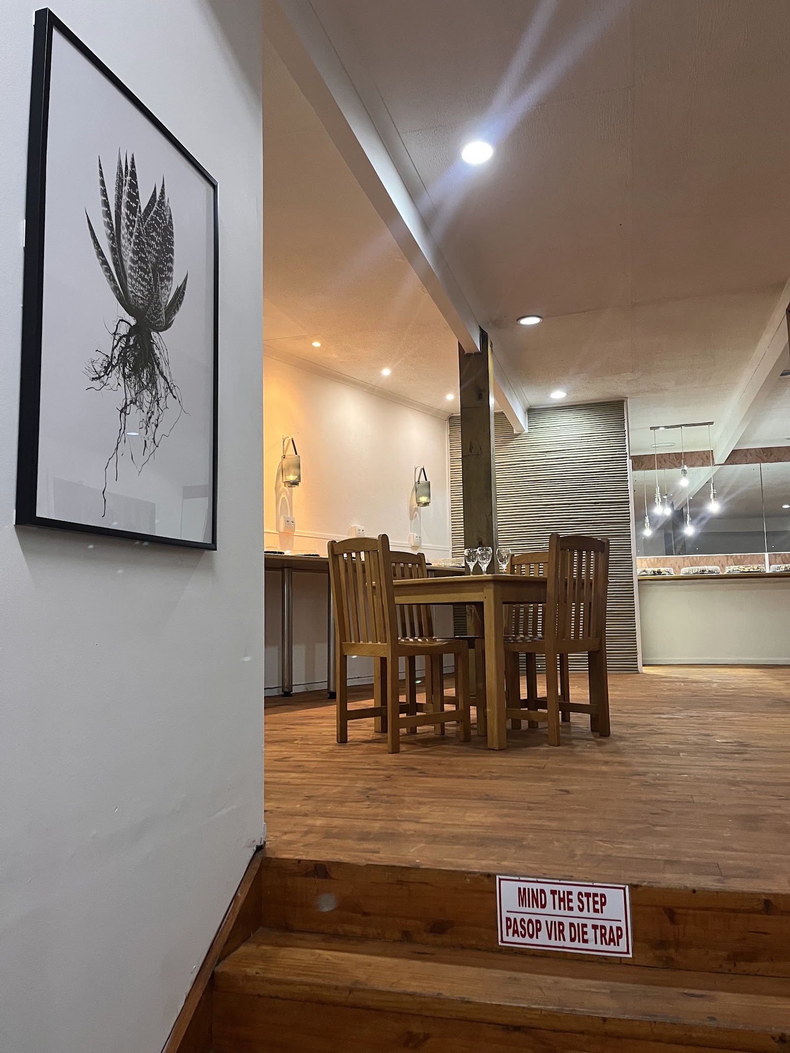 Upscale interior showroom with wooden furniture, framed botanical artwork, pendant lighting, and display cases.