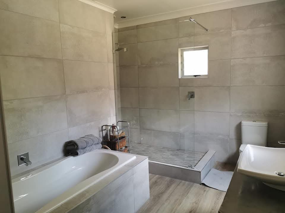 Modern bathroom renovation showing tiled walls, glass shower enclosure, bathtub, and toilet.