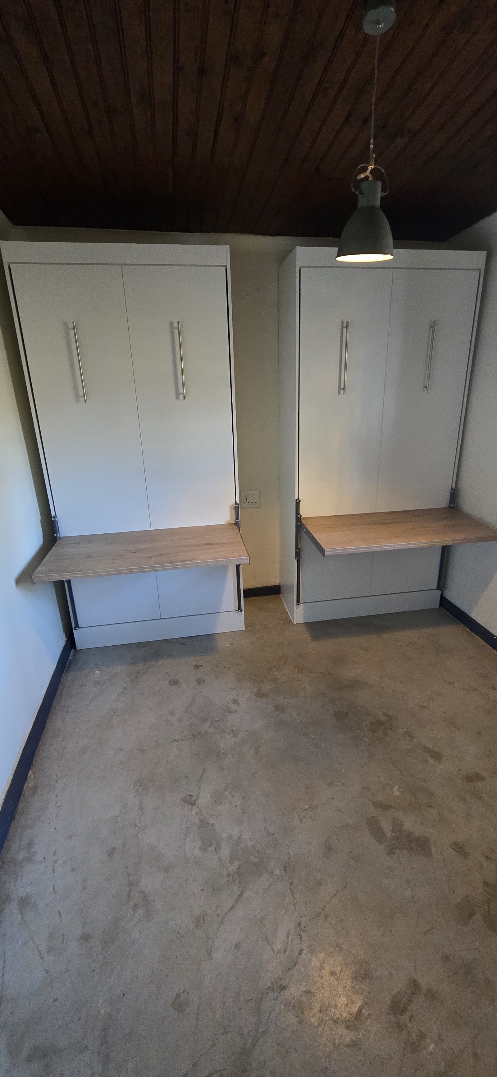 Custom built-in cabinetry with white doors, wood benches, dark wood ceiling, and concrete flooring in storage space.