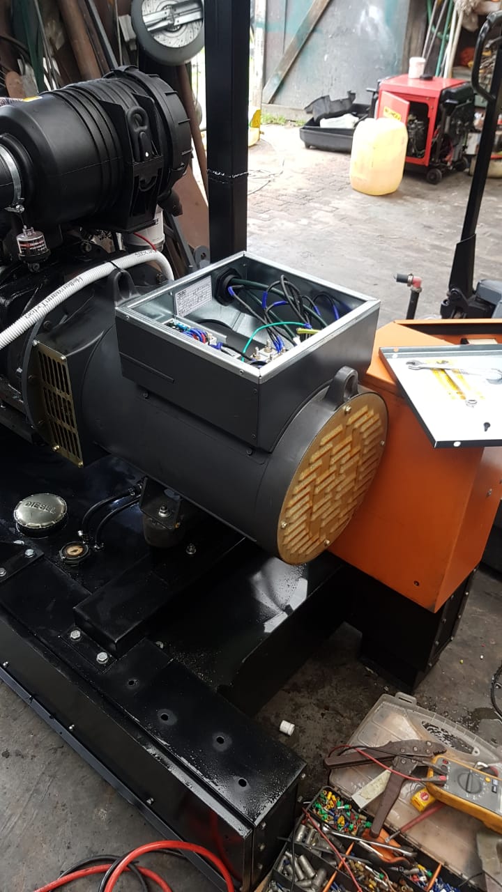 Black diesel generator with orange frame showing internal wiring and control box on workshop floor.