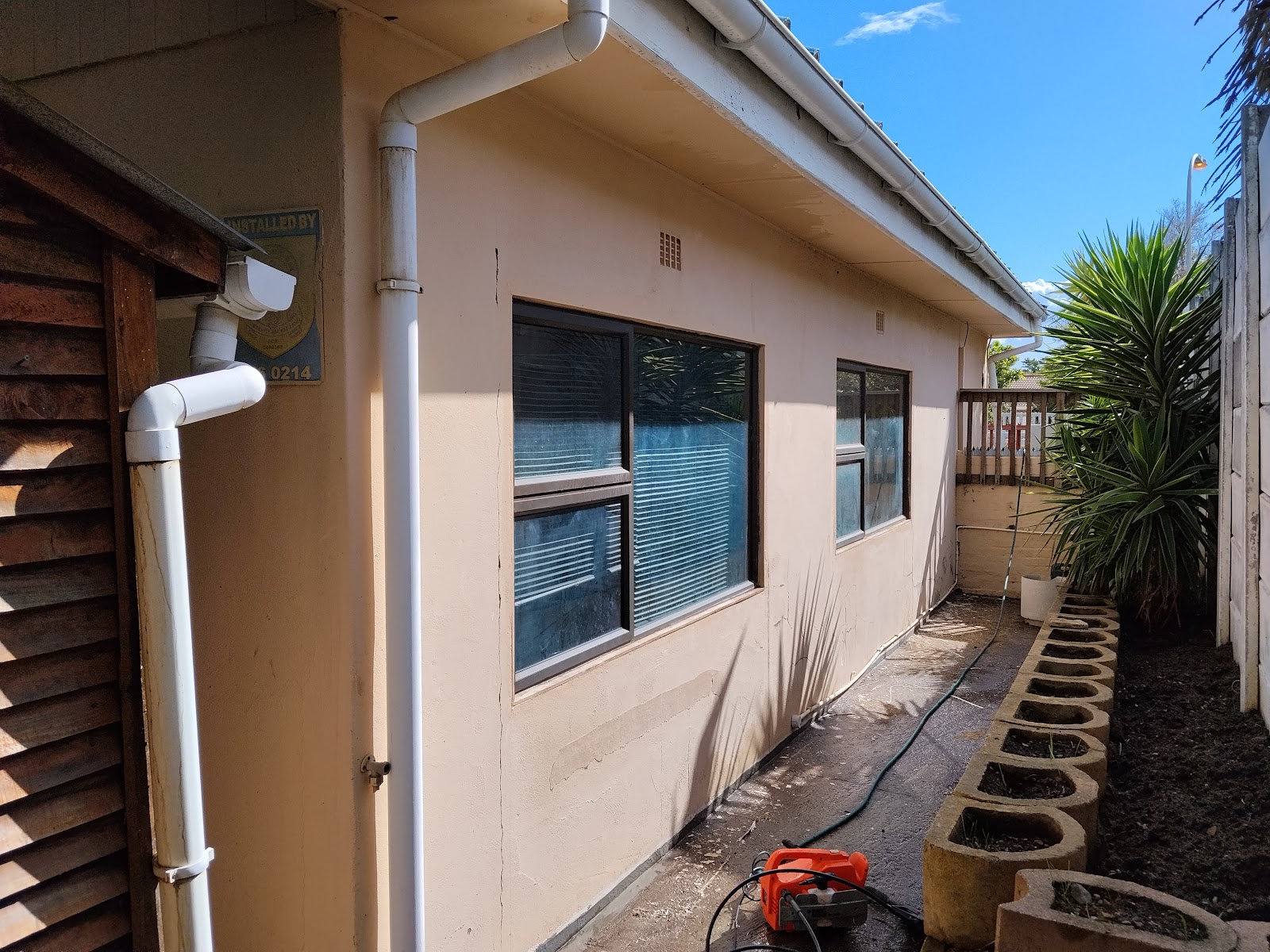 Exterior renovation site showing white PVC piping, weathered timber siding, and power tools on ground.