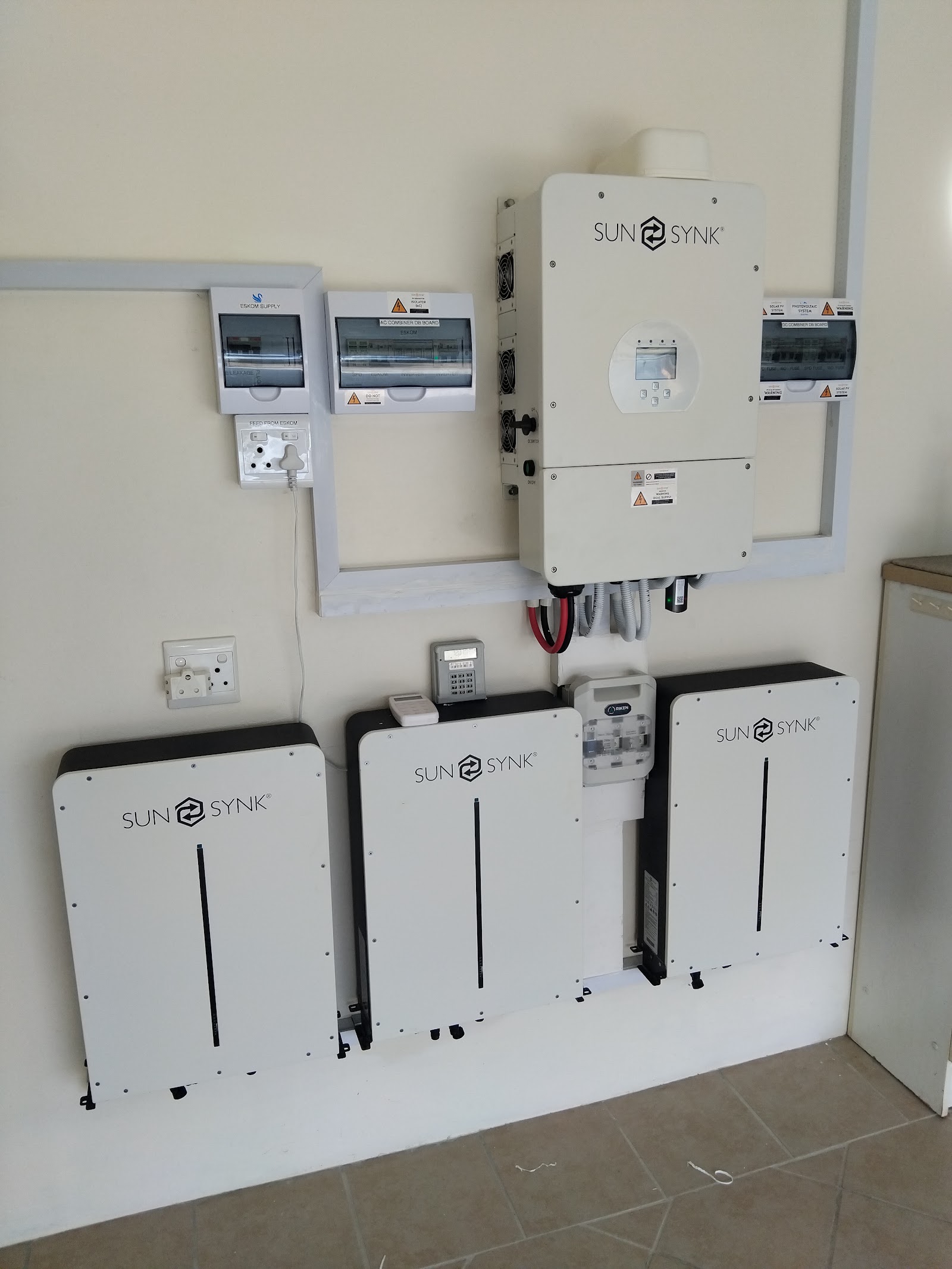 SunSynk battery storage and inverter system installed on interior wall with multiple white units and circuit breakers.