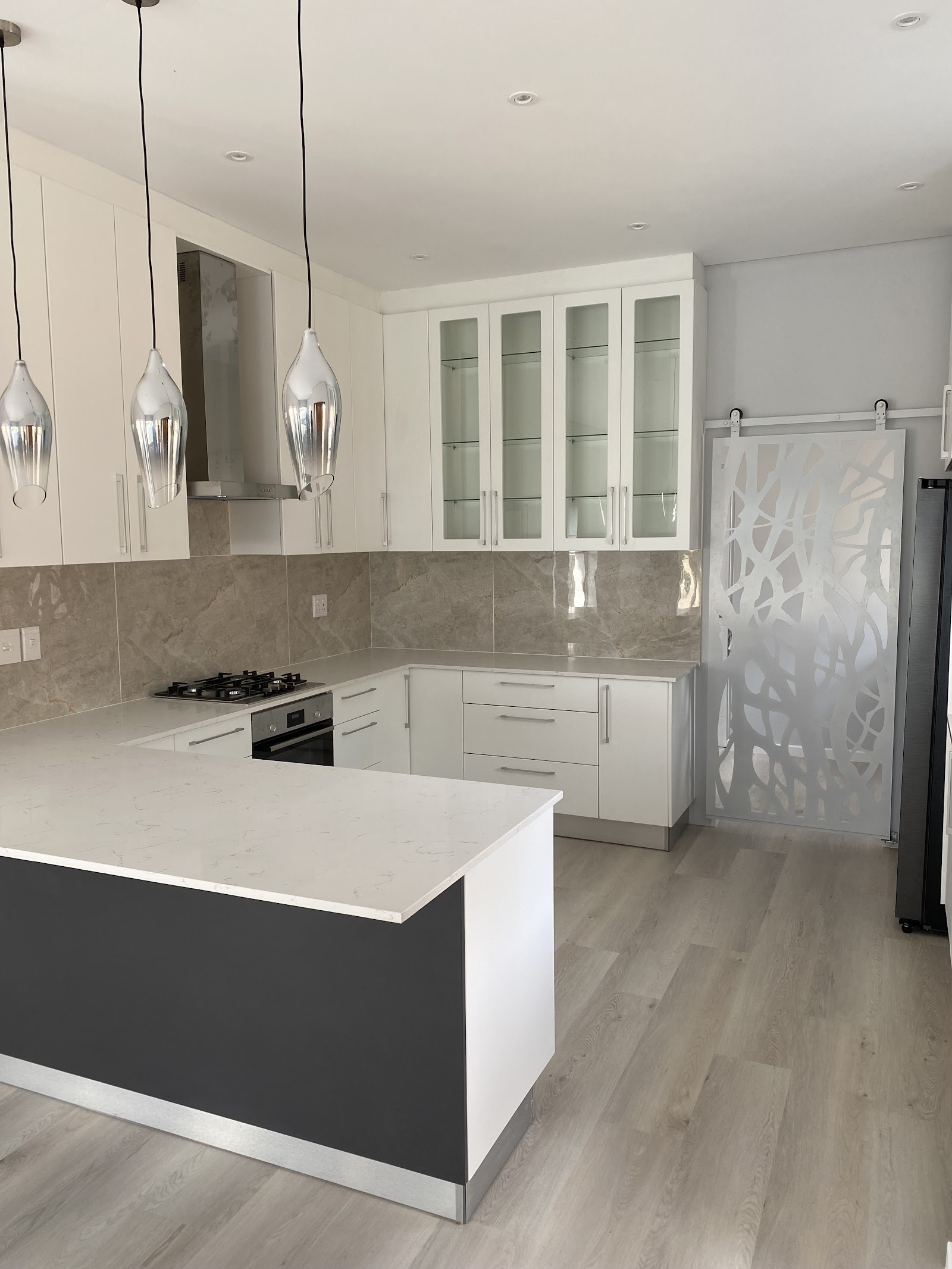 Modern kitchen installation with white cabinetry, gray tile backsplash, gas cooktop, island with black base, and pendant lighting.