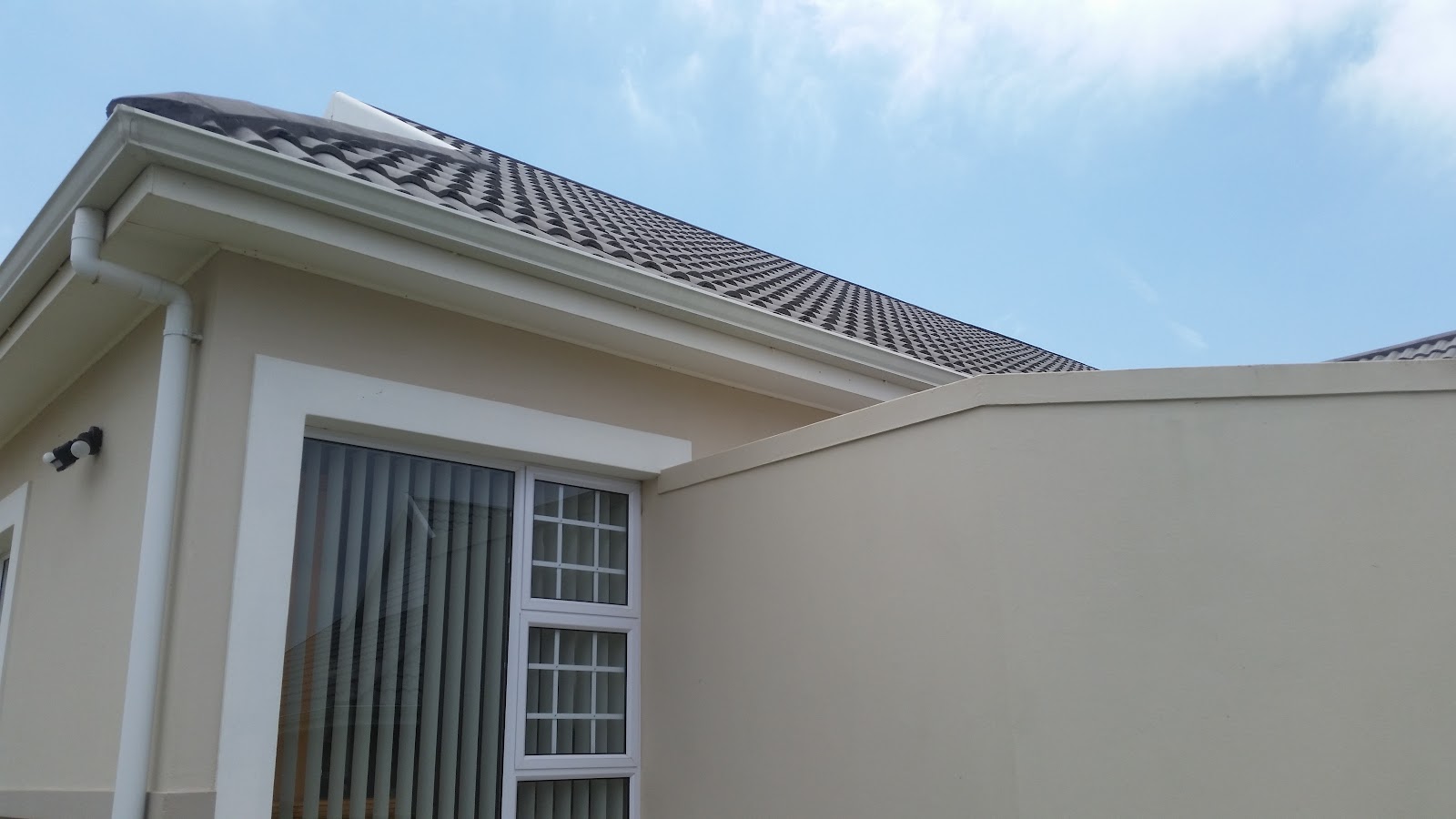 Newly installed black tile roof and white guttering on residential home addition.