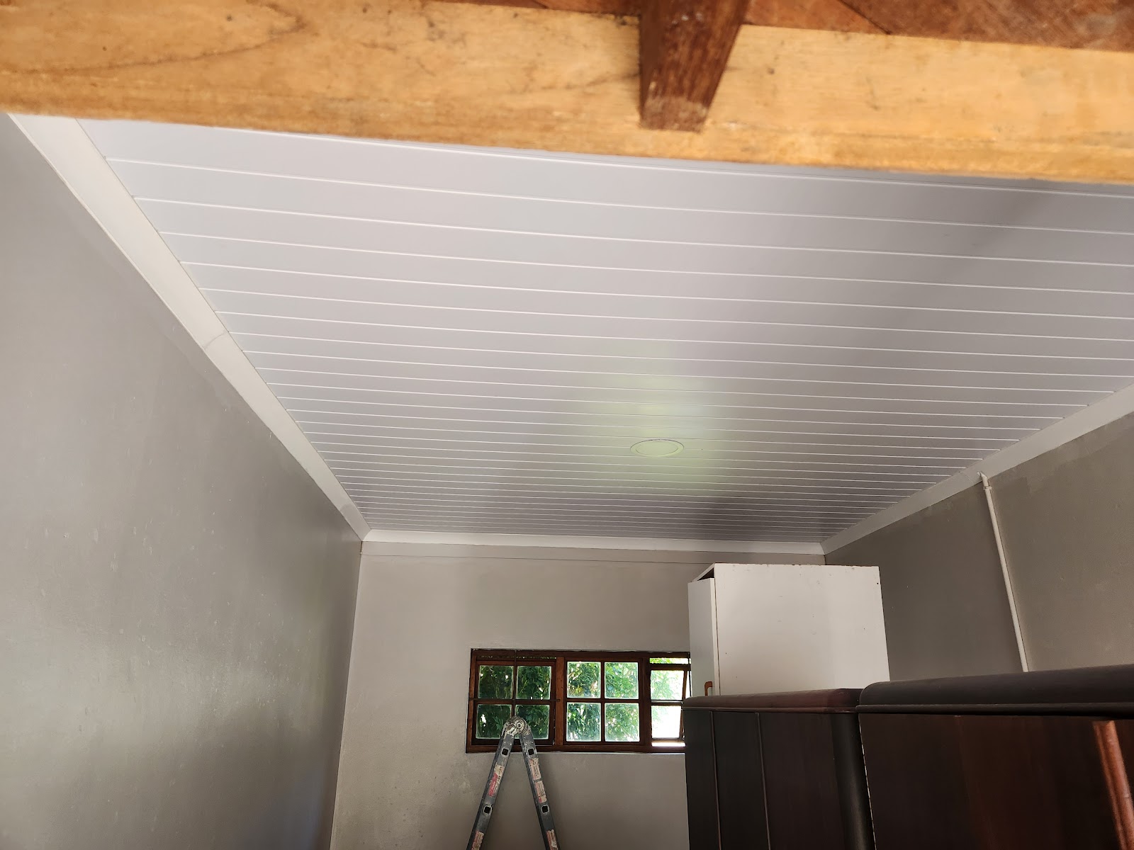 White ribbed ceiling installation with wooden beam detail and ladder in room.