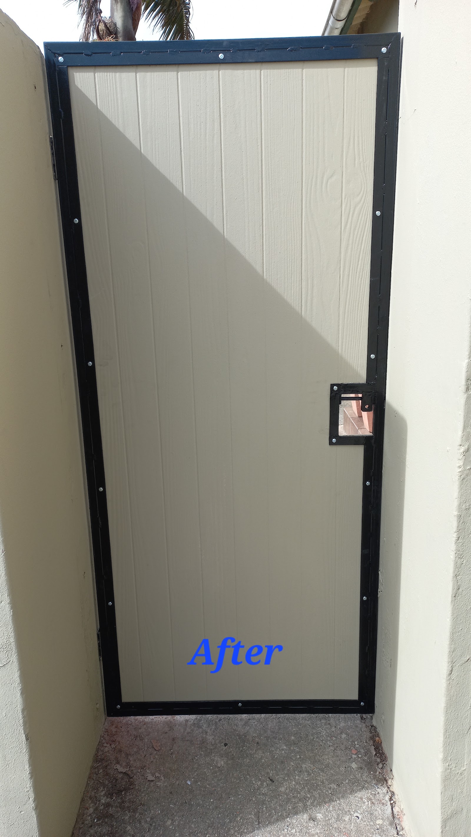 Completed black-framed gate with white corrugated panel and small access door installed.