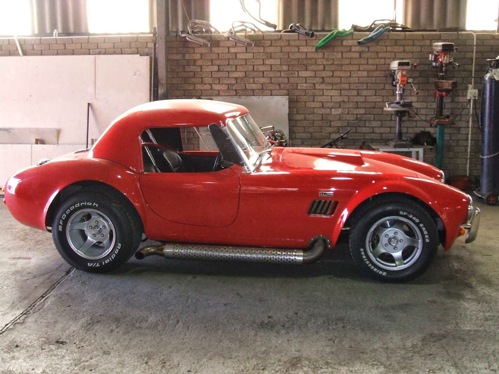 Red Cobra sports car with custom exhaust system in workshop with equipment wall.