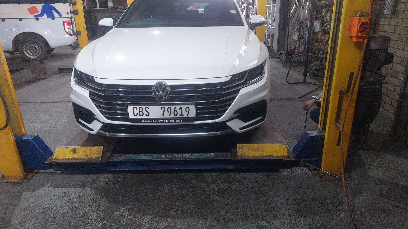 White Volkswagen Passat on two-post lift equipment in service bay.