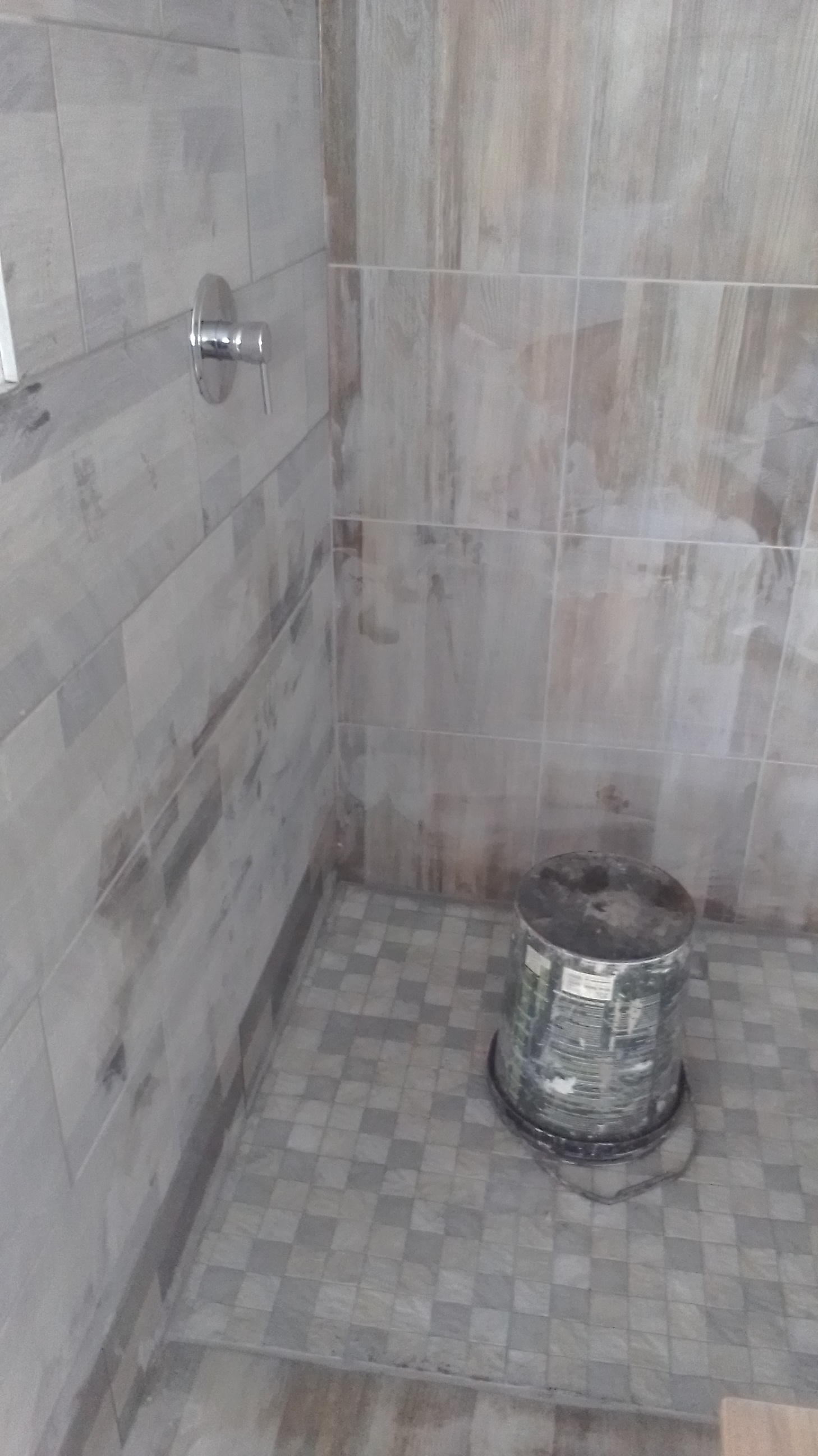 Shower enclosure under construction with gray marble-look tile walls and exposed plumbing fixtures.
