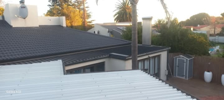 Completed roof installation with dark shingle roof, white metal fascia, and brick chimney on residential property.