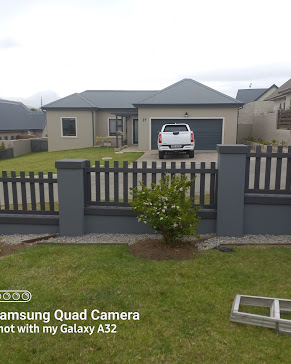 Modern single-story home with beige exterior, dark garage, and gray fence with parked white vehicle.