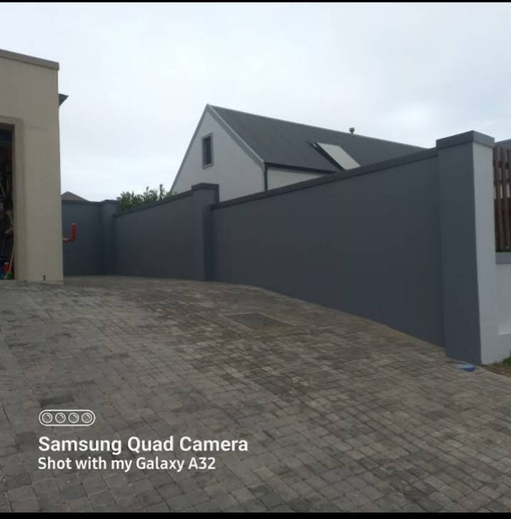 Completed paving project showing dark slate wall, paved driveway with brick pattern, and modern residential architecture.