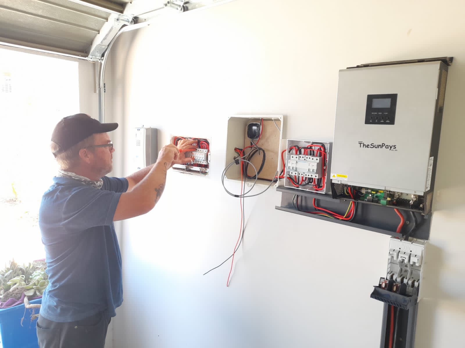 Technician servicing TheSunPays solar inverter system with red wiring and multiple connection terminals.