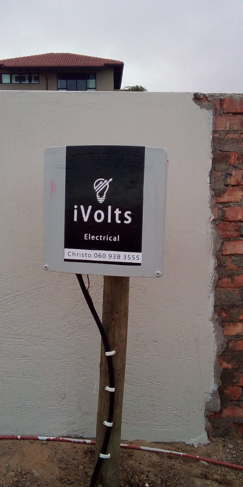 iVolts Electrical service sign with contact information mounted on white wall beside red brick.