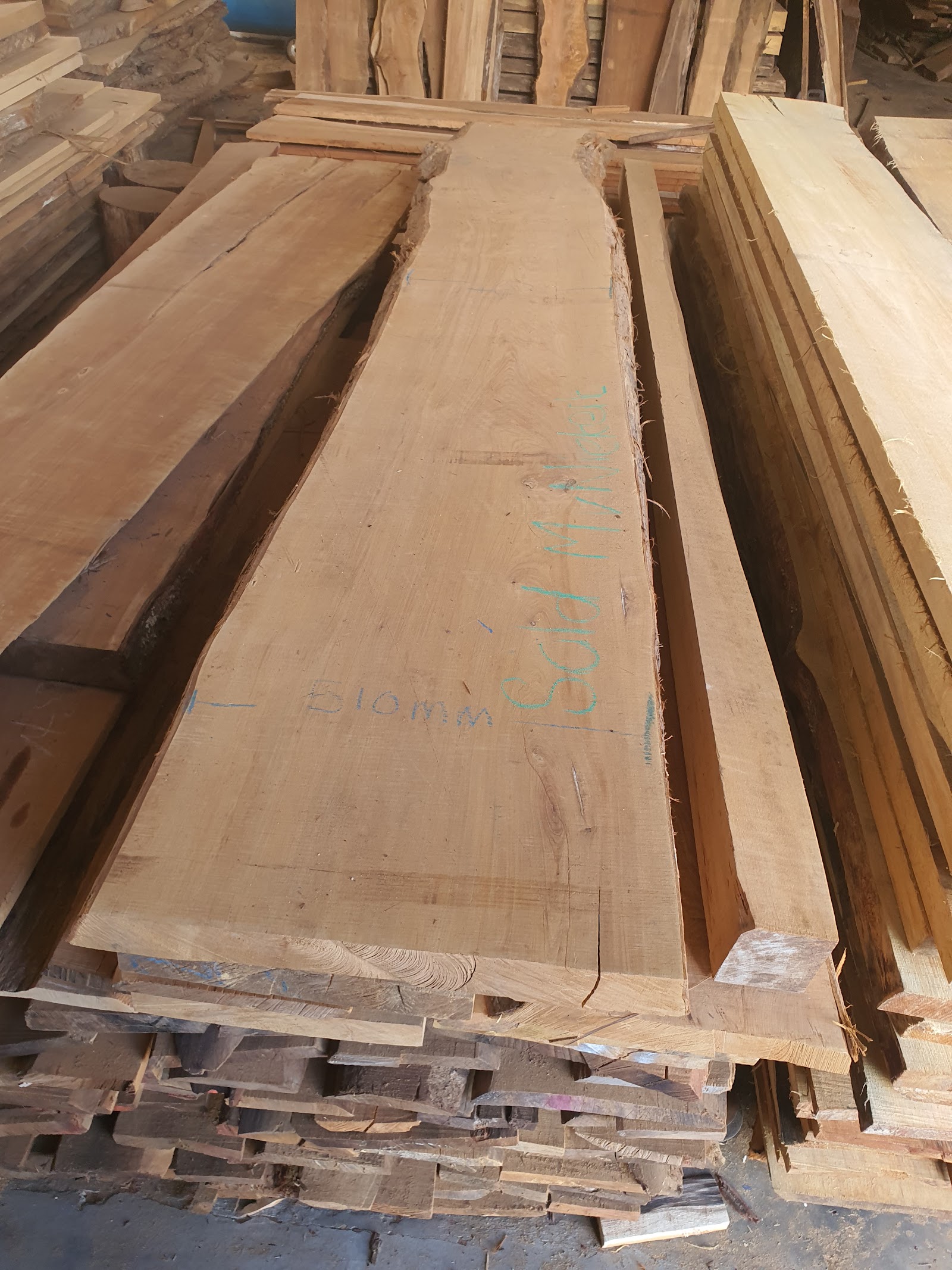 Stacked wooden planks with blue markings in warehouse or storage facility.