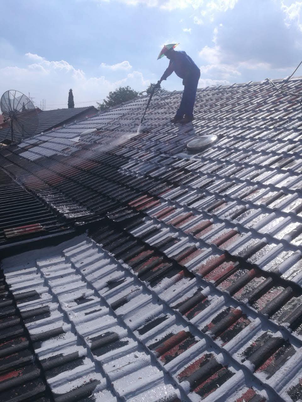 Worker applying sealant to clay tile roof with pressure washing equipment visible.
