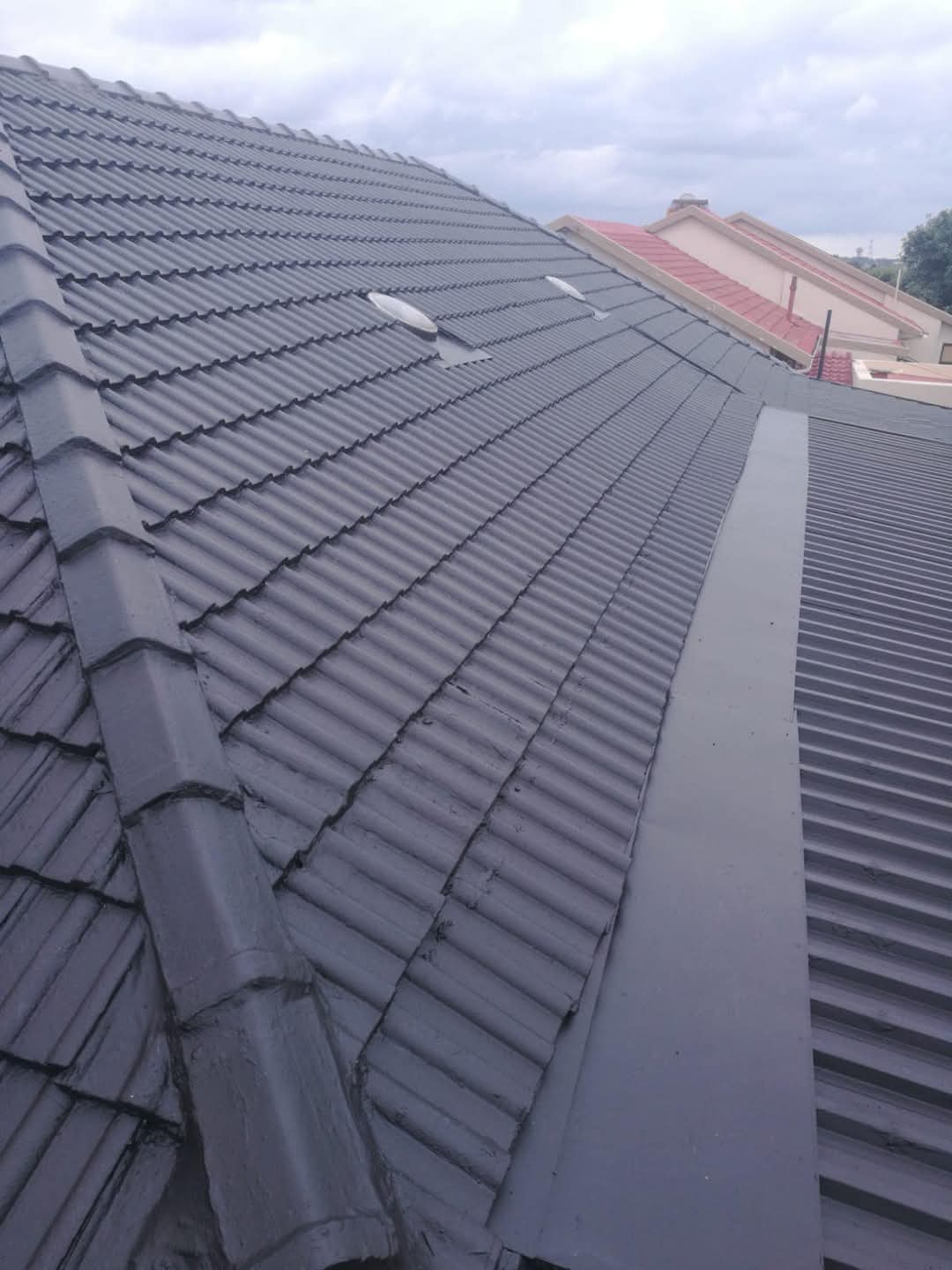Newly installed grey metal roof panels with red tile roofs on neighboring residential buildings.