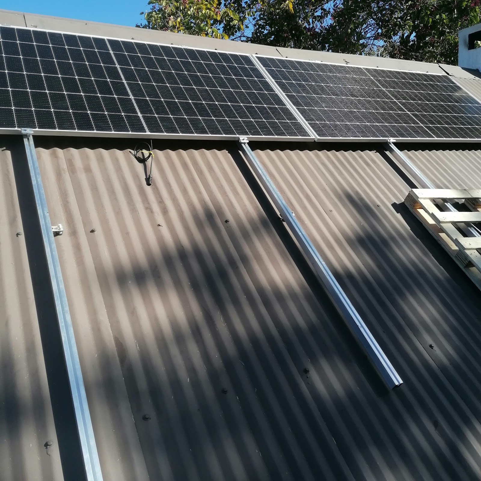 Multiple solar panels mounted on corrugated metal roof structure in daylight.