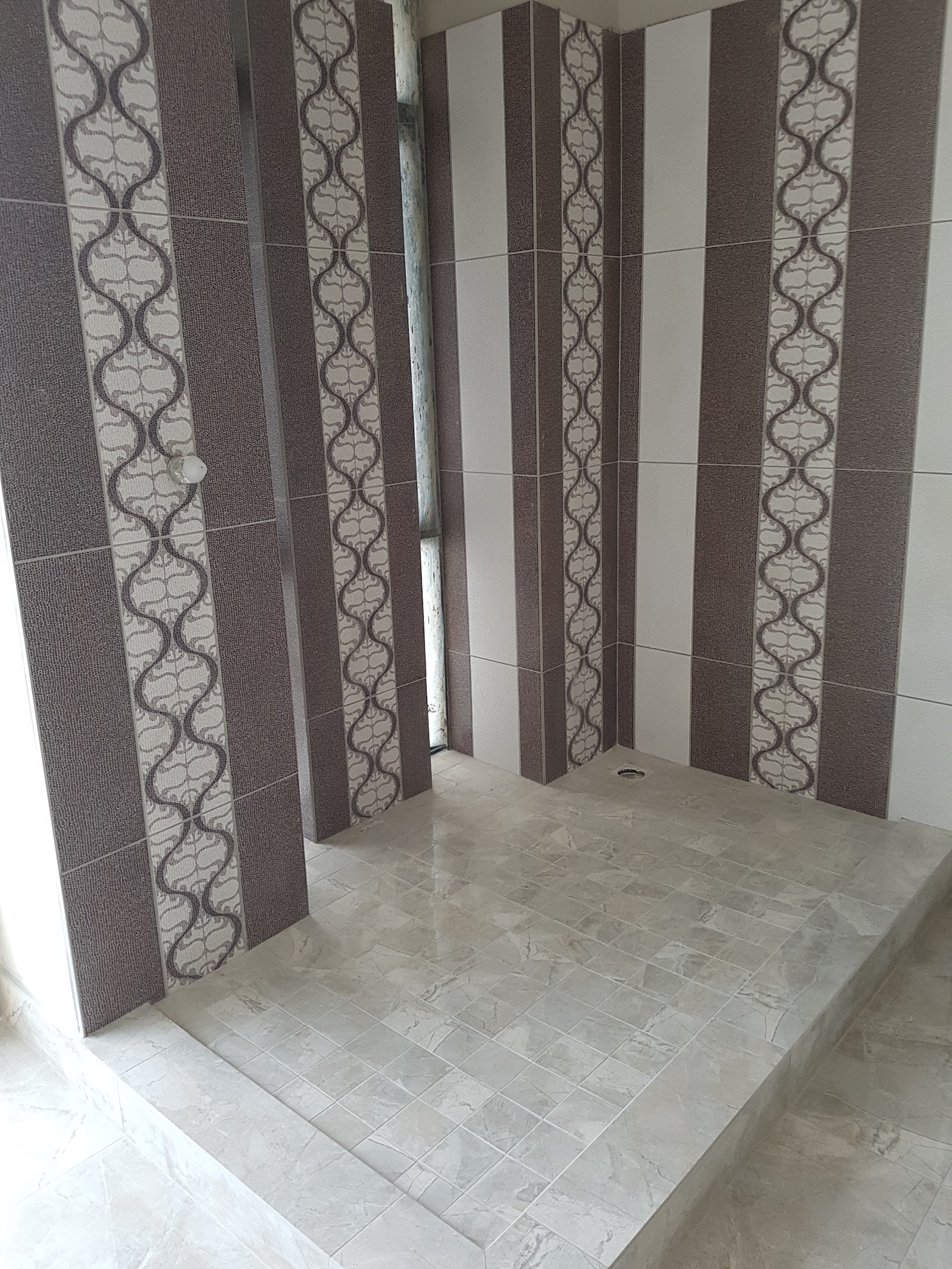 Shower space with dark and cream patterned tile walls and light floor.