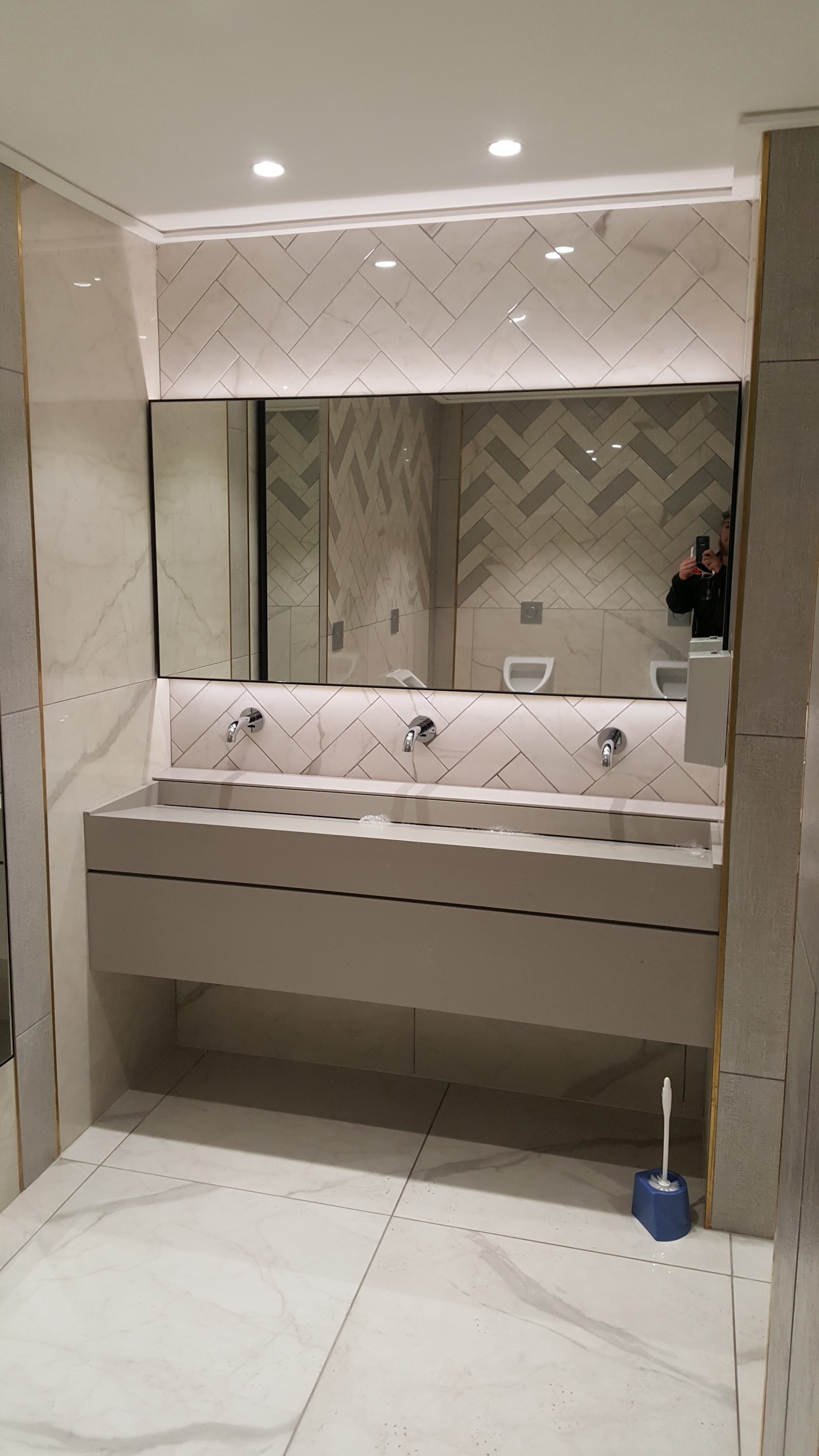 Bathroom vanity with herringbone backsplash, triple faucets, and mirror cabinet.