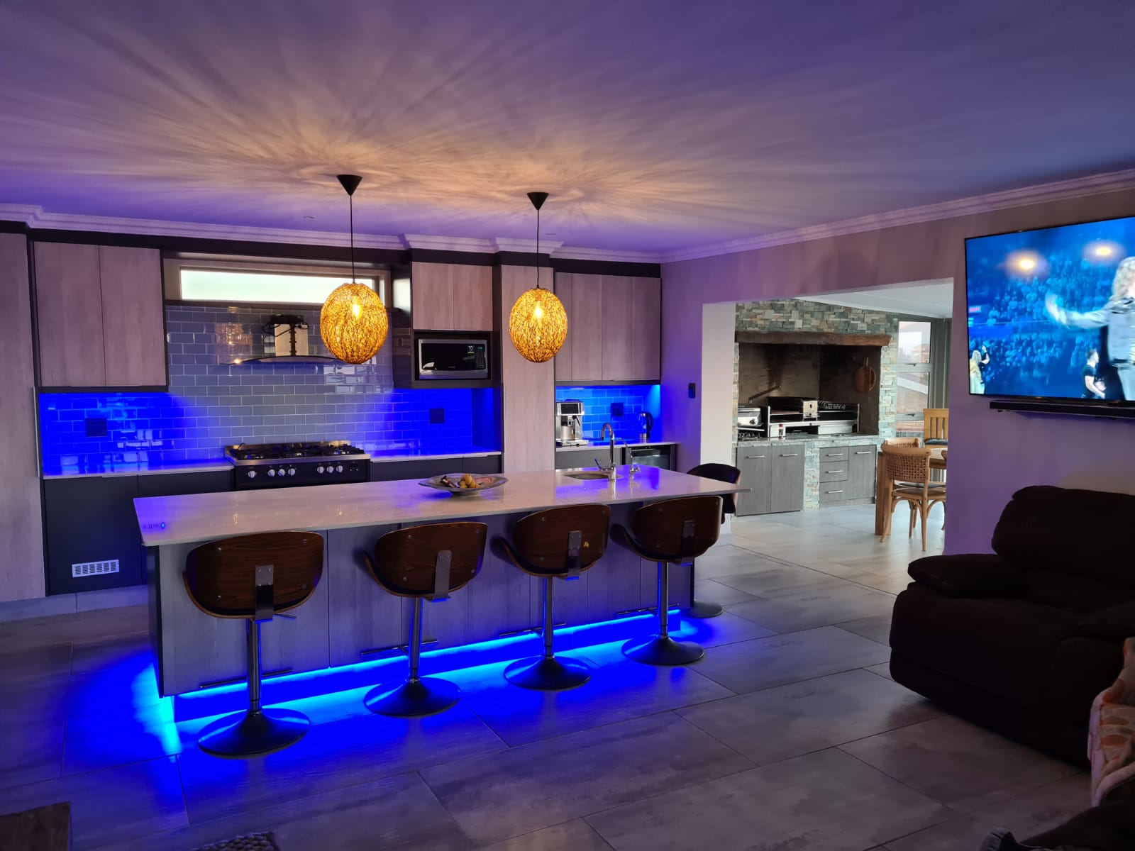 Contemporary kitchen with purple ambient lighting, gold pendant lights, blue backsplash, two islands.