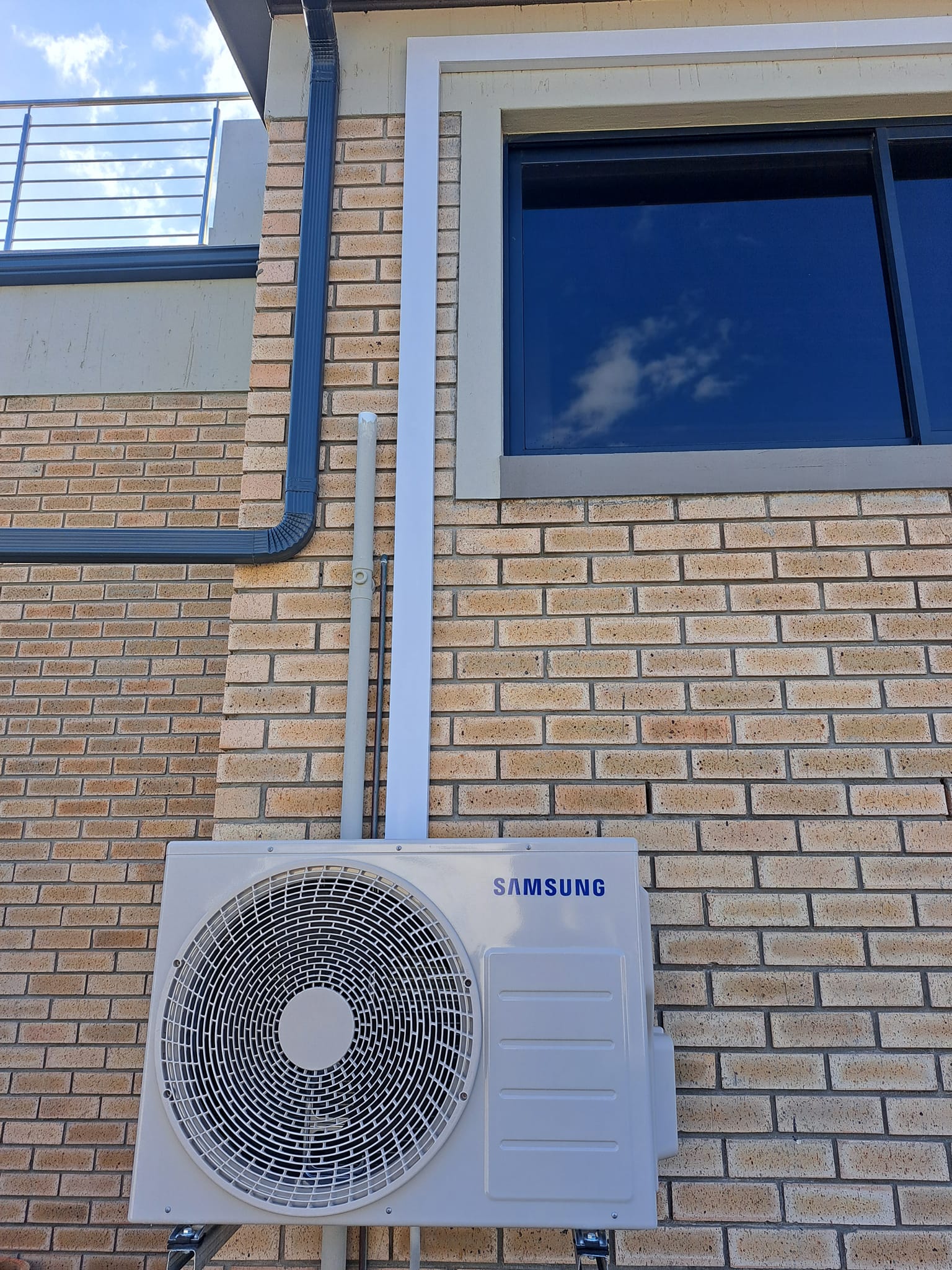 Samsung air conditioning outdoor unit mounted on brick wall with white PVC piping.