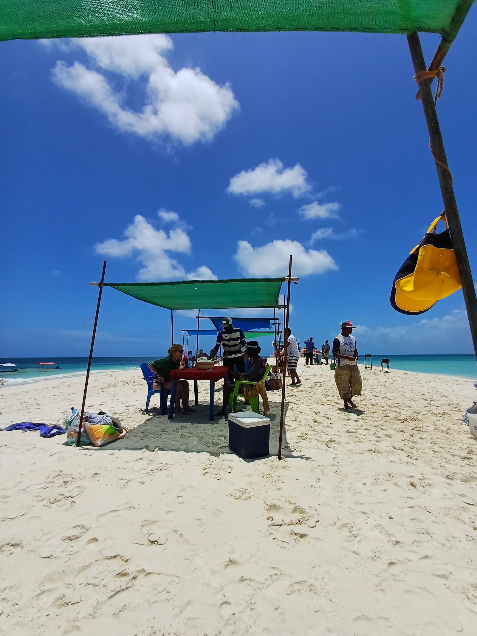 Beach service setup with green and blue shade canopies, tables, staff, and tourists on white sand.