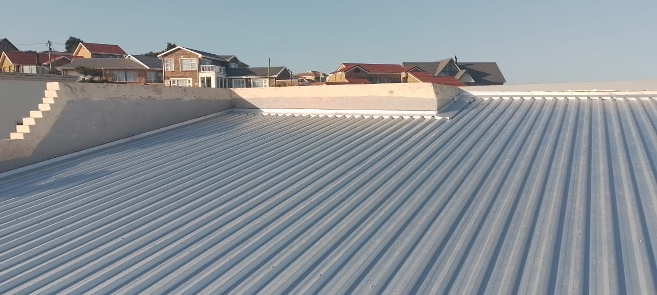 Completed corrugated metal roof installation on residential building with suburban homes visible.