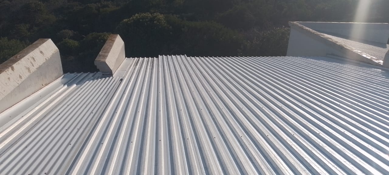 New metal corrugated roof with concrete parapet walls and forested background.