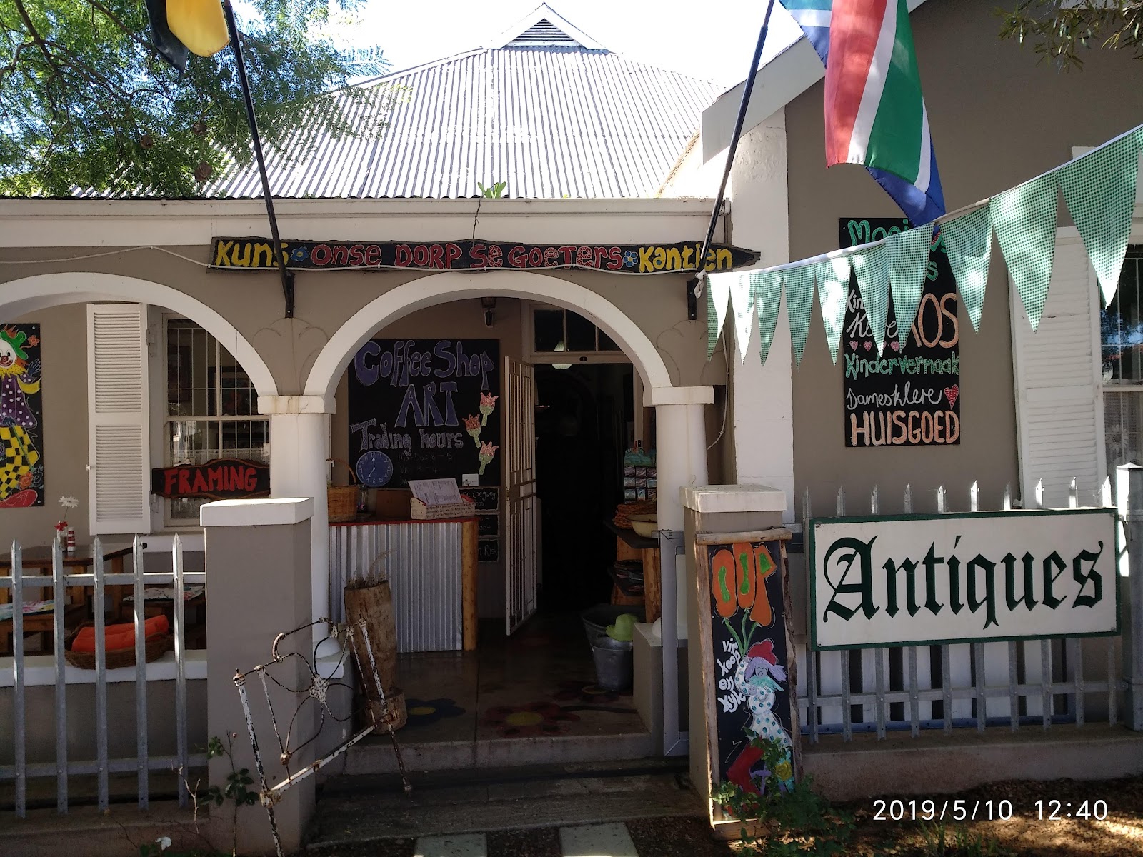 Colonial-style building with "Antiques" sign, coffee shop signage, colorful artwork, and arched white facade.