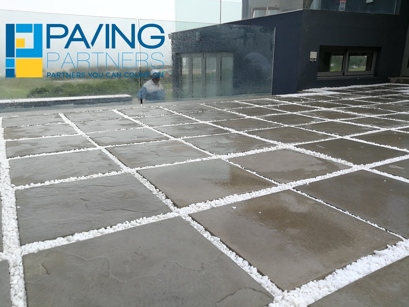 Paving Partners logo visible on modern patio with large concrete pavers and white grout lines.