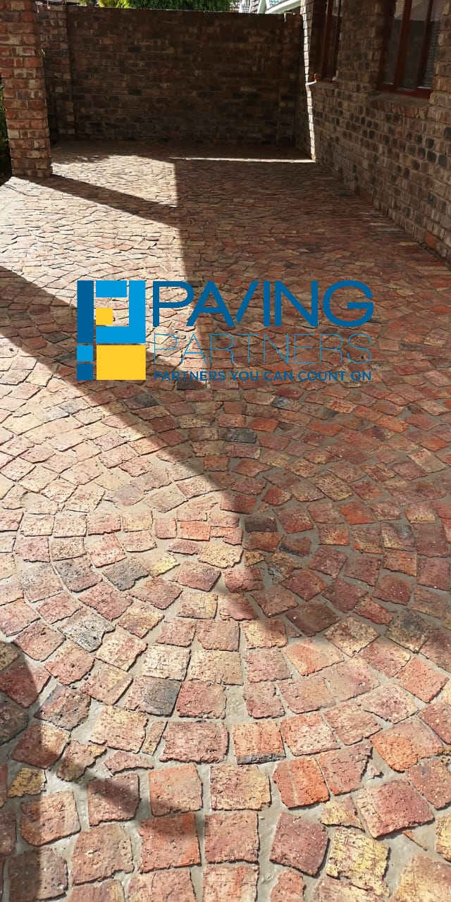 Paving Partners logo on completed red brick herringbone driveway in residential courtyard setting.