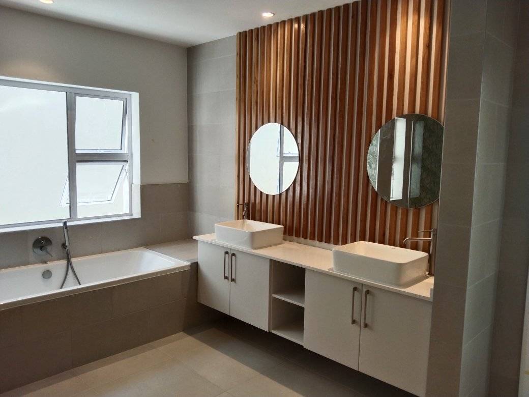Modern bathroom featuring white cabinetry, dual round mirrors, vertical wood slat accent wall, and soaking bathtub.