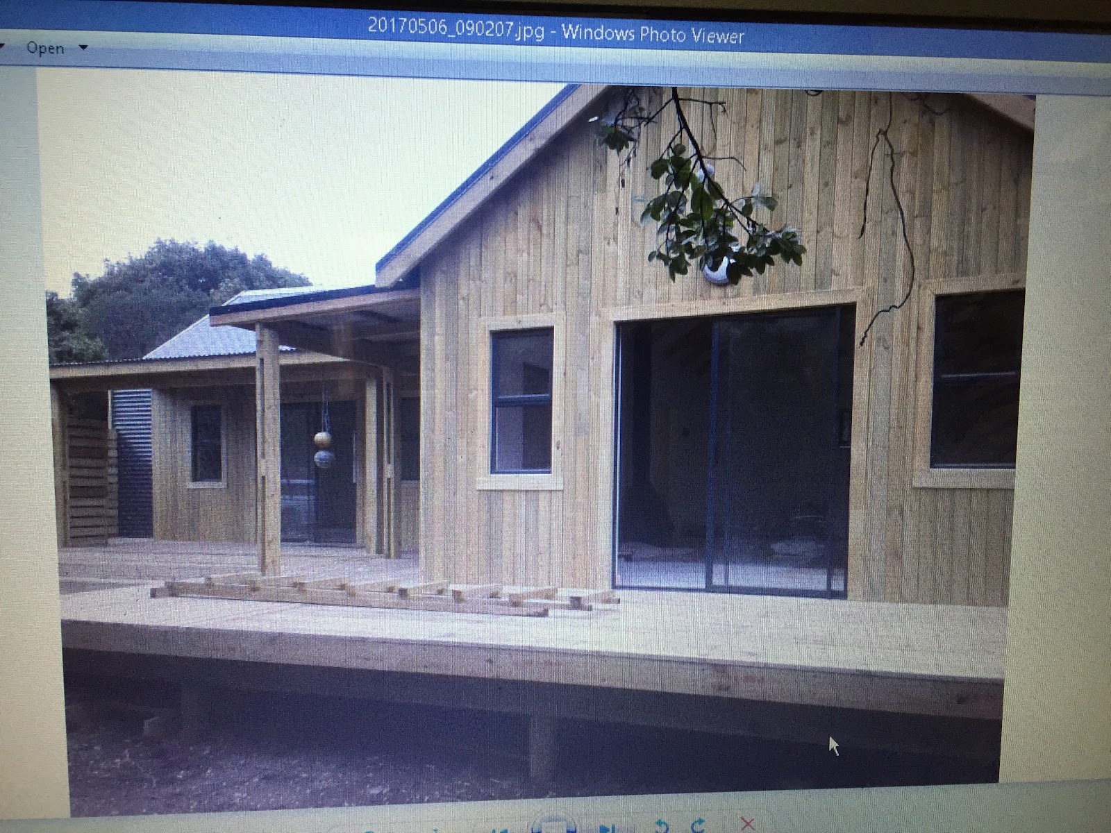 Completed wooden residential structure with metal roof, large windows, and covered porch area in landscaped setting.