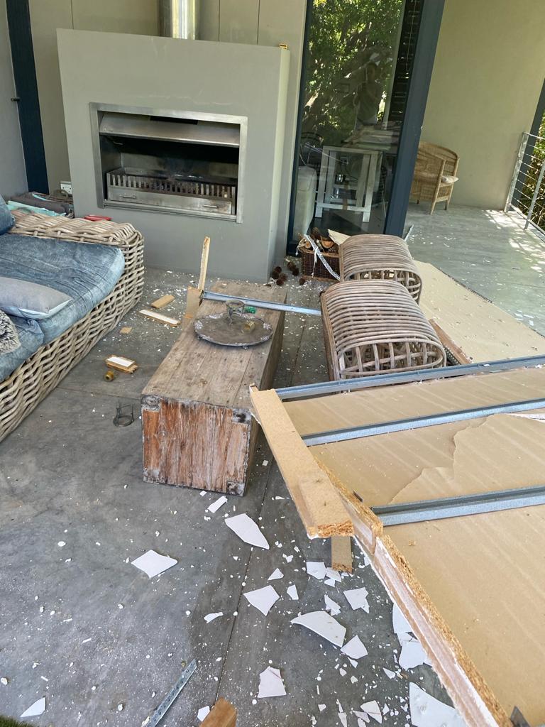 Indoor-outdoor patio space with white fireplace feature, wicker furniture, and construction materials scattered on concrete.