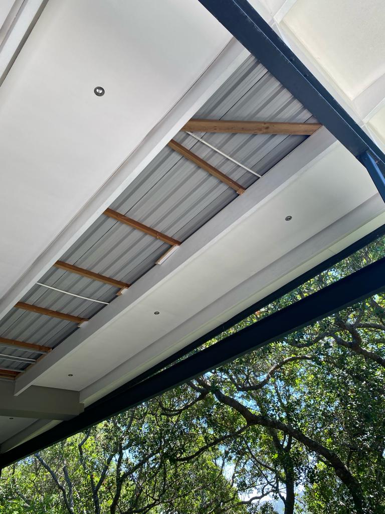 Overhead view of corrugated metal and white drywall ceiling with wooden beams and dark blue fascia trim.