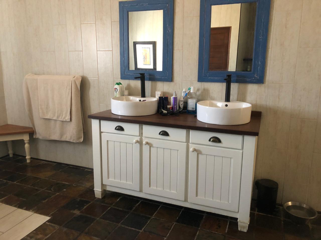 Dual white vessel sinks with blue-framed mirrors on custom vanity with dark countertop and hardware.