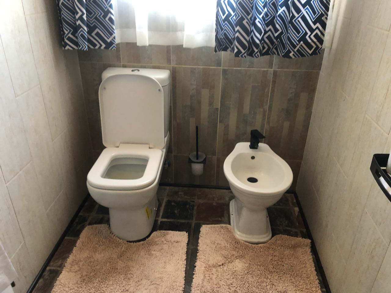 Completed bathroom with toilet, bidet, wood-look tile walls, and patterned window treatments.