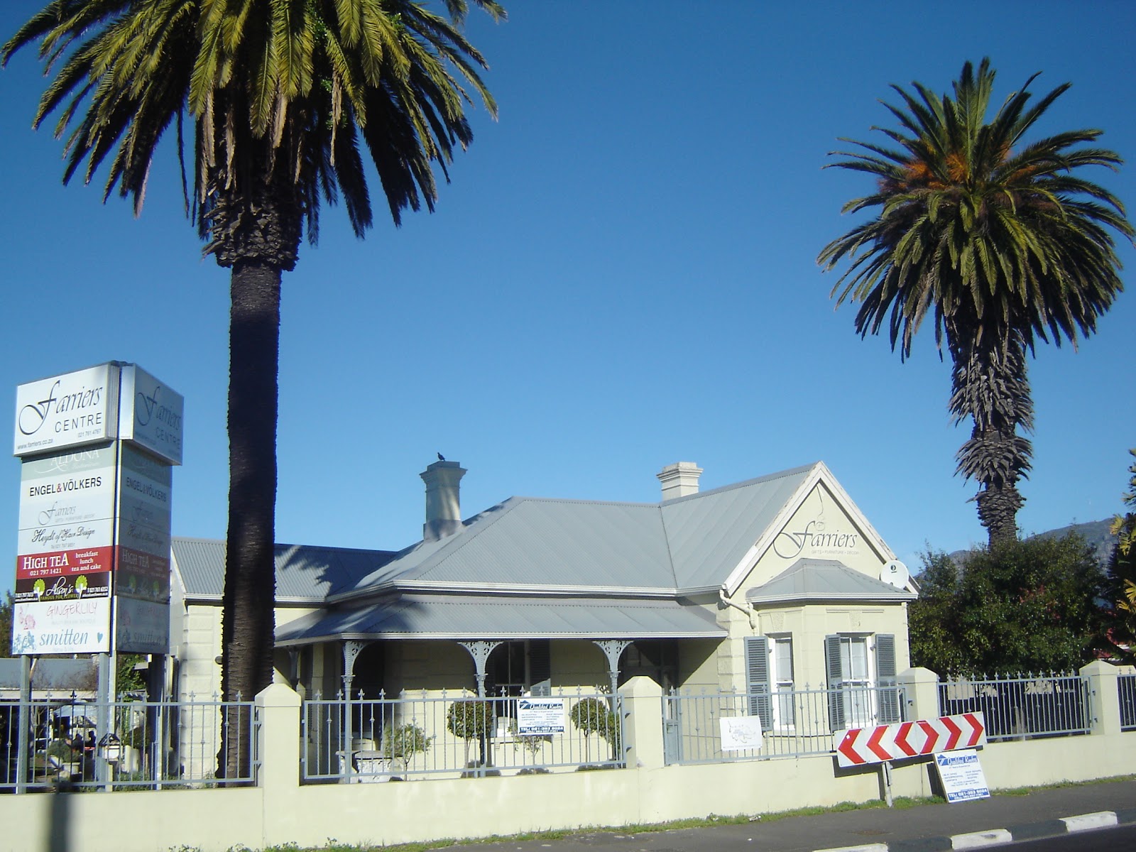 Farmers Centre building with "Farmers" signage, white facade, metal roof, palm trees, fenced front entrance.